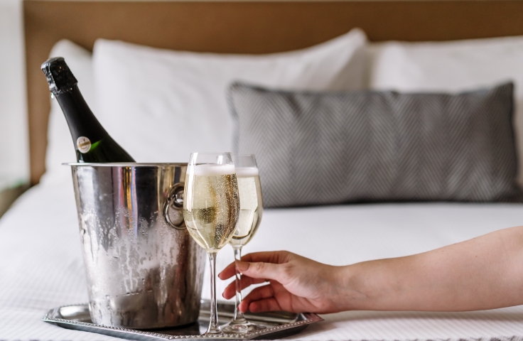 A silver tray with glasses and a bottle of champagne in an ice bucket on a hotel bed.