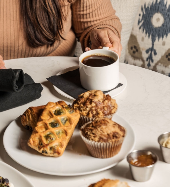 A woman having a coffee and breakfast pastries at a table.